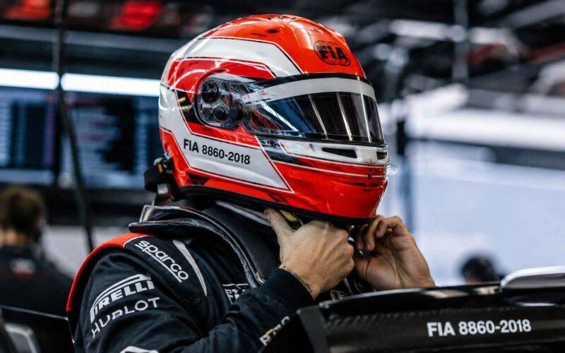 Vue rapprochée d'un pilote en combinaison Sparco, Hublot, Pirelli ajustant son casque rouge et blanc marqué FIA 8860-2018.